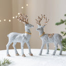 Two decorative deer figurines with glittery antlers and gold necklaces on a snowy surface, Obroi