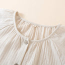 Close-up of a beige garment with a buttoned neckline on a light background, Obroi