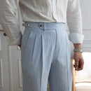 Person wearing light blue pleated pants and a white shirt indoors.