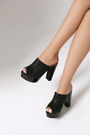 Black glitter platform mule heels with block heels, shown on a model's feet against a light gray studio background, Obroi