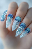 Close-up of a hand with long almond-shaped nails decorated with blue jellyfish and white bubble designs on a glossy translucent base, Obroi