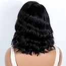 Back view of a person wearing a black wavy wig with shoulder-length waves, shown against a plain light background, Obroi