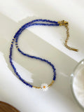 Blue beaded necklace with a gold clasp on a white dish, Obroi