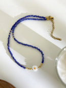 Blue beaded necklace with a gold clasp on a white dish, Obroi