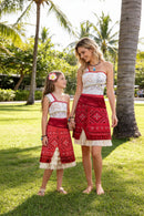 Two women in matching red and white dresses standing on grass with palm trees in the background, Obroi