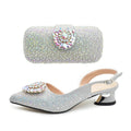 Silver high-heeled shoes and matching clutch with rhinestone embellishments on a white background, Obroi