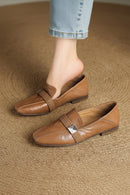 Brown loafers with decorative straps worn by a person on a textured brown surface, Obroi