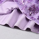 Close-up of a purple fabric with sequin details on a light gray background, Obroi