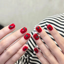 Nails with red polish and green dots resembling tomatoes, against a blurred background, Obroi