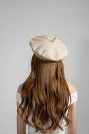 Person wearing a beige beret with long brown hair on a gray background, Obroi