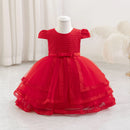 A bright red toddler girl's party dress displayed on a white mannequin dress form. The dress features a textured honeycomb pattern bodice, short puff sleeves, a matching red satin bow at the waist, and a tiered tulle skirt with embroidered lace trim, Obroi
