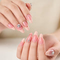 Close-up of hands with long almond-shaped nails painted in a glossy light pink shade, with two nails decorated with small silver rhinestone clusters, against a soft beige background, Obroi
