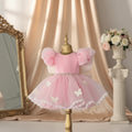 A pink toddler girl's party dress displayed on a gold dress form mannequin. The dress features a solid pink bodice, voluminous puff sleeves made of sheer pink organza, a beaded waistband, and a layered tulle skirt decorated with white butterfly appliqués and a white lace hem, Obroi