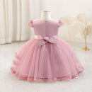 A pink toddler girl's party dress displayed on a mannequin, featuring a solid pink bodice with lace cap sleeves, a matching pink satin bow at the back waist, and a layered tulle skirt with lace trim, Obroi