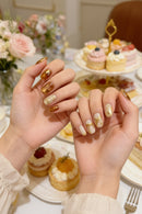 Close-up of hands with decorative nail art against a background of pastries and flowers, Obroi