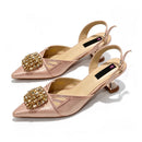 A pair of pointed-toe slingback kitten heels in metallic rose gold, featuring a large gold rhinestone embellishment on the vamp and a low metallic gold heel, shown on a white background, Obroi