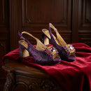 Purple high-heeled shoes with decorative embellishments on a red fabric surface, Obroi