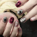 Close-up of hands with decorative nail art featuring red, silver, and pink designs.