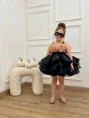 Young girl in a black and peach dress standing in a room with white walls and wooden floor, Obroi
