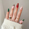 Close-up of a hand with green, red, and gold nail polish wearing rings on a neutral background, Obroi