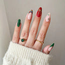 Close-up of a hand with green, red, and gold nail polish wearing rings on a neutral background, Obroi
