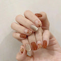 Hand with intricately designed nails featuring gold and brown colors on a neutral background, Obroi