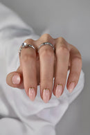 Hand with pink nail polish and silver rings on a neutral background, Obroi