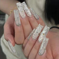 Nails with decorative white and gold designs on a neutral background, Obroi