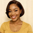 A smiling woman with a short dark brown bob haircut wearing a yellow scoop-neck t-shirt and a delicate gold necklace, set against a plain beige background, Obroi