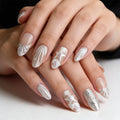 Close-up of a hand with decorative silver nail art on a neutral background, Obroi