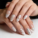 Close-up of a hand with decorative silver nail art on a neutral background, Obroi