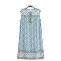 A sleeveless A-line nightgown dress with a light blue and purple floral pattern, featuring a tie-neck design with tassels and decorative borders at the neckline and hem, hanging on a wooden hanger against a white background, Obroi