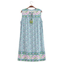 A sleeveless A-line nightgown dress with a light blue and purple floral pattern, featuring a tie-neck design with tassels and decorative borders at the neckline and hem, hanging on a wooden hanger against a white background, Obroi