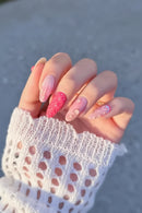 Hand with pink and white floral nail design against a blurred background, Obroi