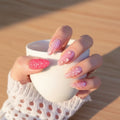 Hand with pink and white floral nail design against a blurred background, Obroi
