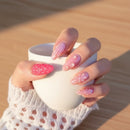 Hand with pink and white floral nail design against a blurred background, Obroi