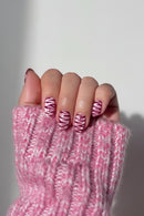 A close-up of a hand with almond-shaped nails painted in a pink and white zebra stripe pattern, resting on a chunky pink knit sweater, Obroi