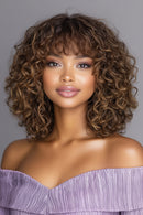 Woman with curly hair wearing an off-shoulder purple top against a gray background, Obroi