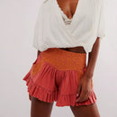 Person wearing a white top and orange ruffled shorts on a plain background, Obroi
