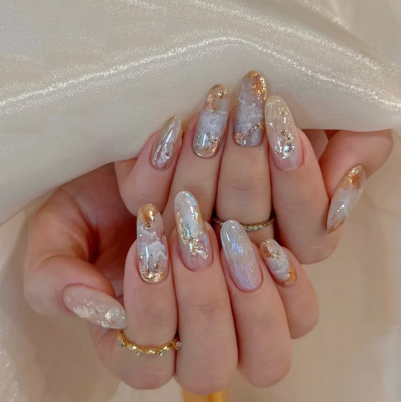 Hand with decorative nails featuring gold and silver glitter on a neutral background, Obroi
