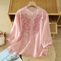 Pink floral blouse on a hanger against a wooden shelf background, Obroi