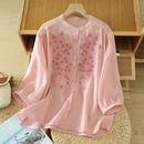 Pink floral blouse on a hanger against a wooden shelf background, Obroi