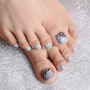 Close-up of toes with gray nail polish and decorative elements on a textured surface, Obroi