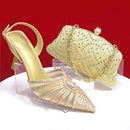 Gold high-heeled shoe and matching handbag with rhinestone details on a red background, Obroi