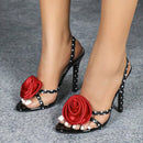Black high-heeled shoes with red floral decorations on a gray background, Obroi