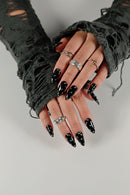 Close-up of hands with black nail polish and multiple rings on a neutral background, Obroi