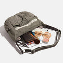 Open olive green backpack with various items on a white background, Obroi