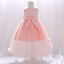 A sleeveless pink girl's party dress displayed on a mannequin, featuring a structured bodice, a large satin bow at the waist, and a layered tulle skirt with a sheer lower overlay, Obroi