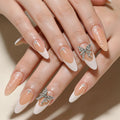 Close-up of a hand with long almond-shaped nails styled in a French manicure, featuring glossy nude-pink bases, white tips, small rhinestone accents, and two silver butterfly decorations, Obroi