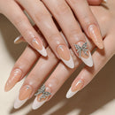 Close-up of a hand with long almond-shaped nails styled in a French manicure, featuring glossy nude-pink bases, white tips, small rhinestone accents, and two silver butterfly decorations, Obroi